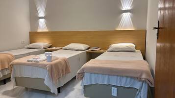 A hotel room with three single beds, each with a wooden headboard and a bedside table.