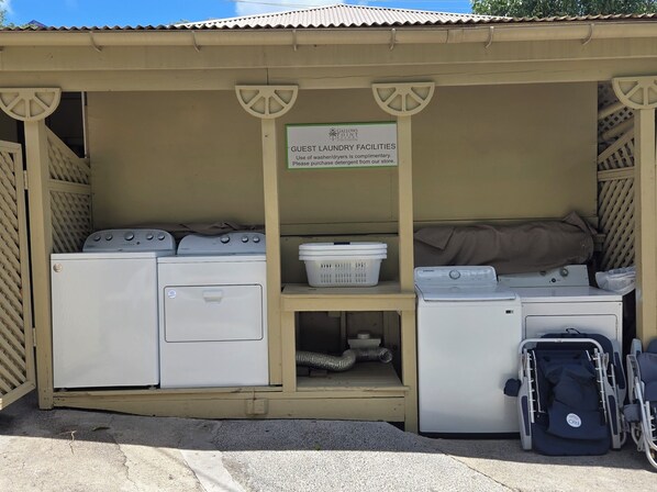 A laundry facility with two washing machines, a dryer, and a sign indicating guest laundry services.