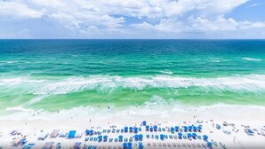A beach with clear turquoise waters, a sandy shore, and numerous blue umbrellas and lounge chairs.