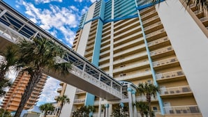 A multi-story hotel with a central walkway connecting the floors, surrounded by palm trees.