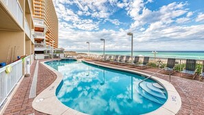 A swimming pool with a curved edge, surrounded by a brick deck and lounge chairs.