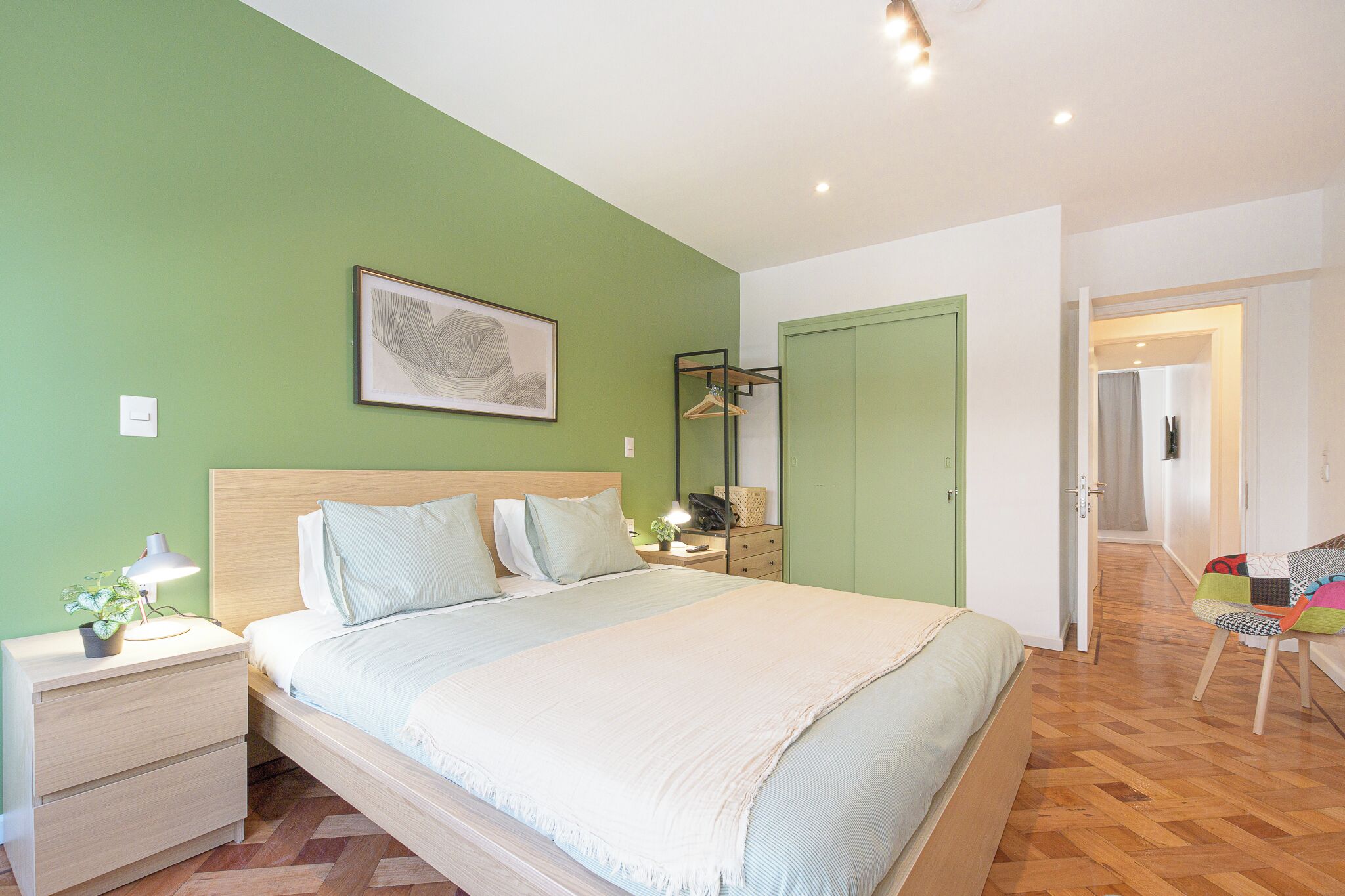 A bedroom with a bed, nightstands, a dresser, a mirror, and a green wall.
