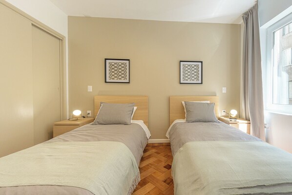 Habitación doble con dos camas, suelo de madera y ventana con cortinas.