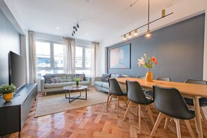 Een moderne woonkamer met een bank, salontafel en een eethoek met stoelen en een houten tafel.