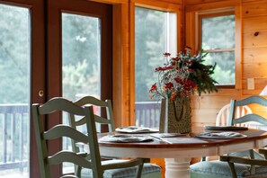 A wooden interior with a round table, chairs, and a vase with flowers.