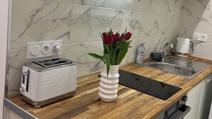 A modern kitchen with white cabinets, a marble backsplash, a toaster, a sink, and a vase with red flowers on the countertop. - Charming apartment (Paris)