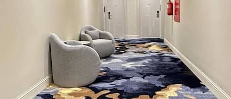 Un pasillo de hotel con alfombra estampada, una lámpara moderna y una fila de puertas.