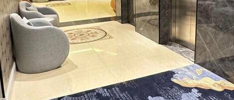 A hotel lobby with a marble floor, a reception desk, and a waiting area with chairs.
