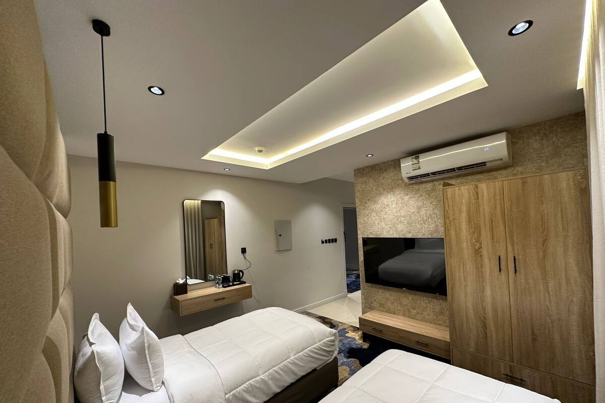 A modern hotel room with two beds, a large mirror, a TV, and an air conditioning unit.