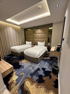 A modern hotel room with two beds, a large mirror, a wooden side table, and a patterned carpet.