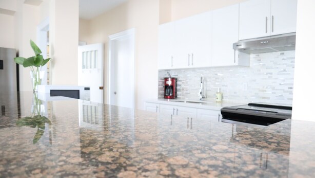Una cocina con encimeras de granito, armarios blancos y una campana extractora de acero inoxidable.