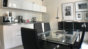 A modern kitchen with white cabinets, a glass dining table, and black chairs. There are kitchen appliances like a microwave, kettle, and toaster. - Old Town Market Sqr. View-Self Check in 24h-VAT incl. (Wrocław)
