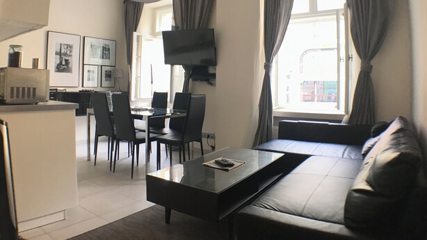 A modern living room with a sofa, a coffee table, a TV mounted on the wall, and a dining area with chairs and a table. - Old Town Market Sqr. View-Self Check in 24h-VAT incl. (Wrocław)