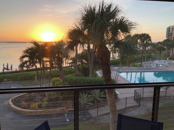 Vista de una piscina con palmeras y un atardecer de fondo.