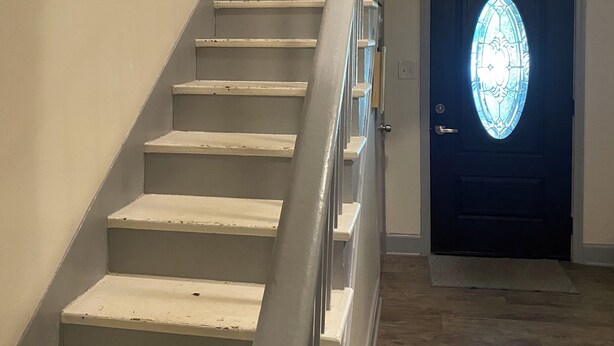 A staircase with a handrail leading to a door with a stained glass window.