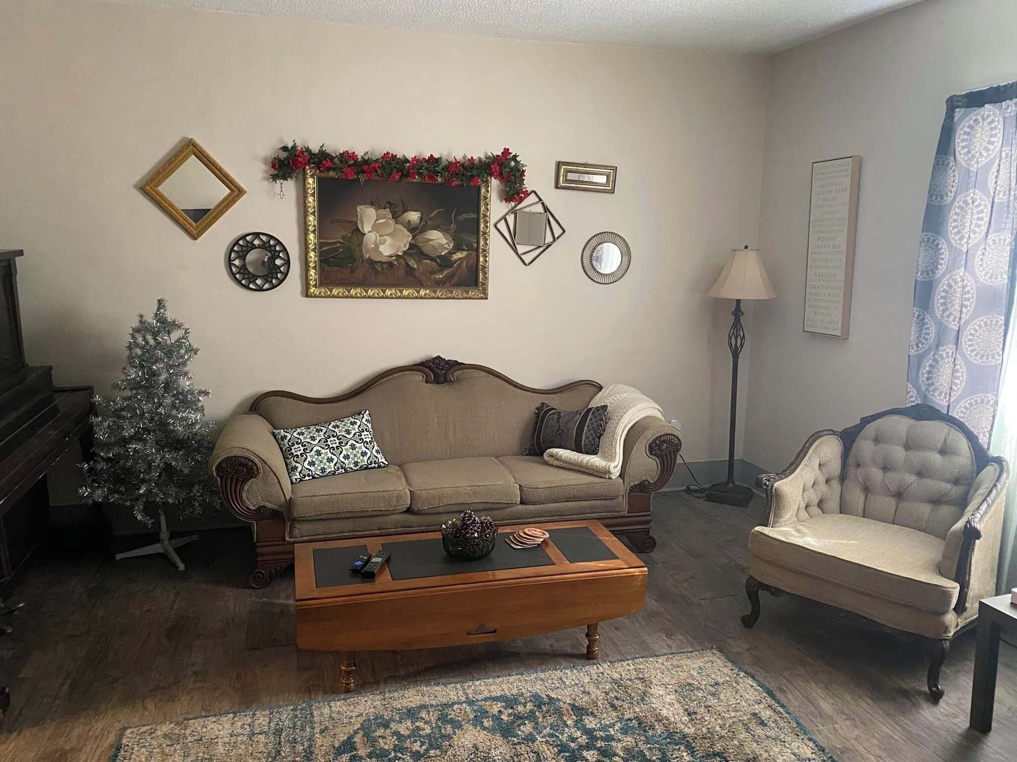 Een woonkamer met een bank, fauteuil, salontafel en een kleine kerstboom.