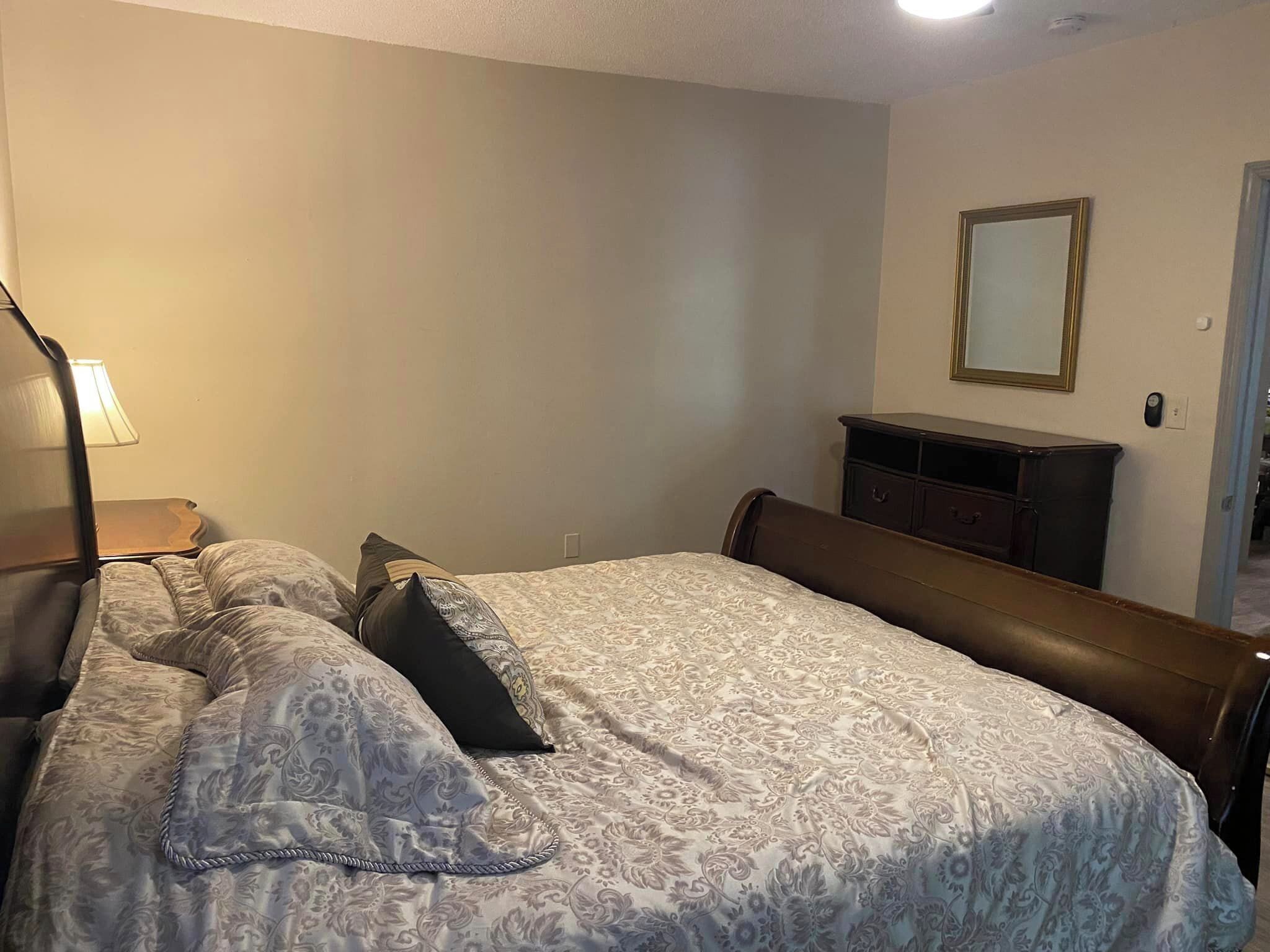 A bedroom with a bed, a nightstand, a dresser, and a mirror on the wall.