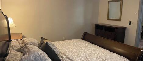 A bedroom with a bed, a nightstand, a dresser, and a mirror on the wall.