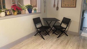 A small dining area with a table and two chairs, a window with plants, and a wall-mounted knife and spoon.