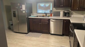 A kitchen with dark wooden cabinets, stainless steel appliances, and a window with blinds.