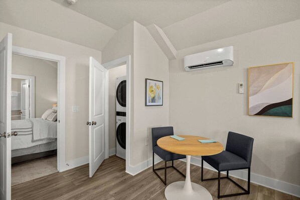 Habitación de hotel con cama, lavadora, mesa de comedor con sillas y equipo de aire acondicionado.