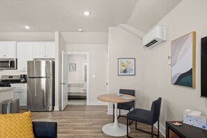 A modern kitchen with stainless steel appliances, a dining area with a round table and two chairs, and a living space with a sofa and a coffee table.