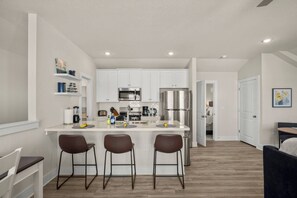 A modern kitchen with white cabinets, a stainless steel refrigerator, and a central island with bar stools. - Austin Brand new Furnished Casita near Tesla (Austin)