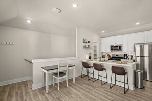 A modern kitchen with white cabinets, a stainless steel refrigerator, and a bar area with stools.
