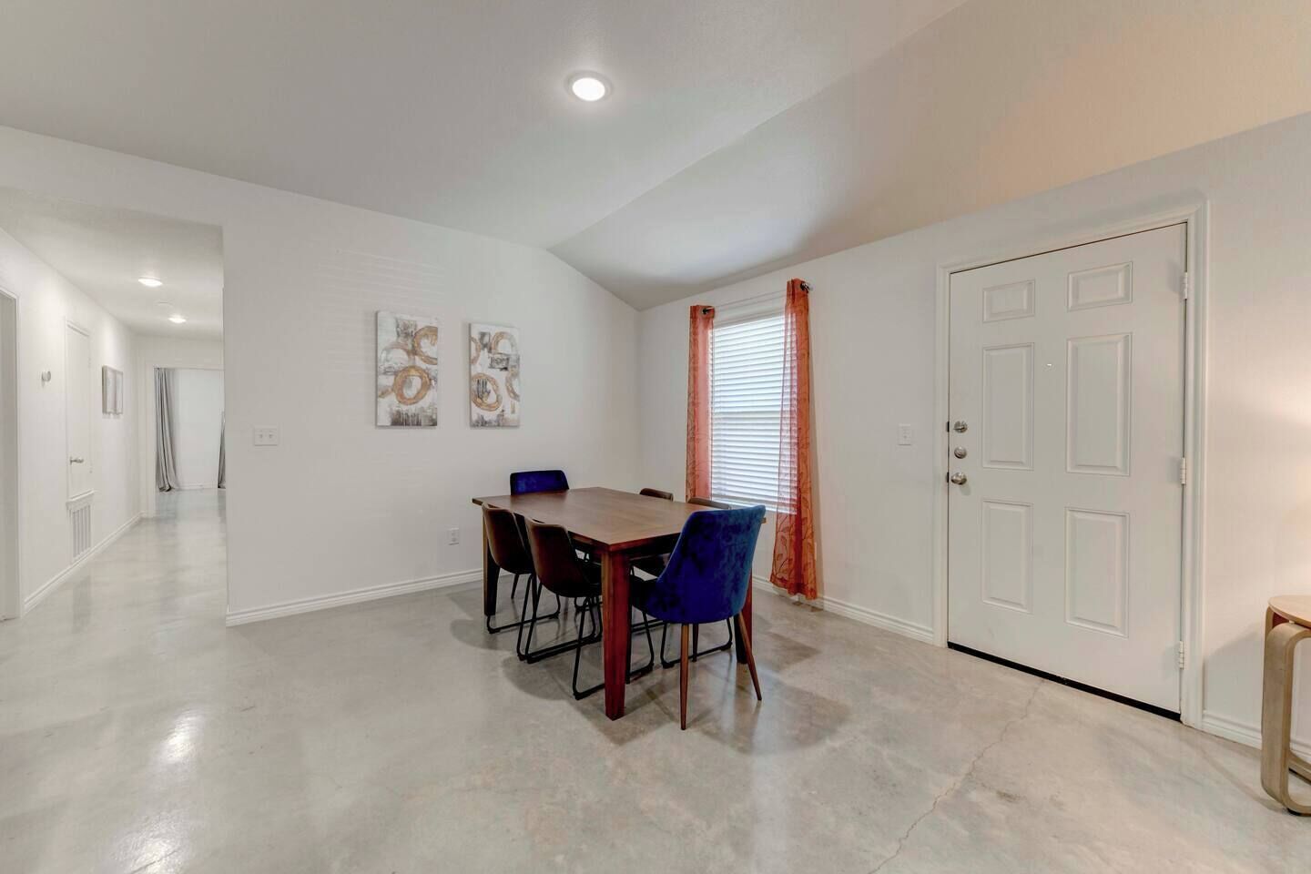 A dining area with a table and chairs, a door, and a hallway.