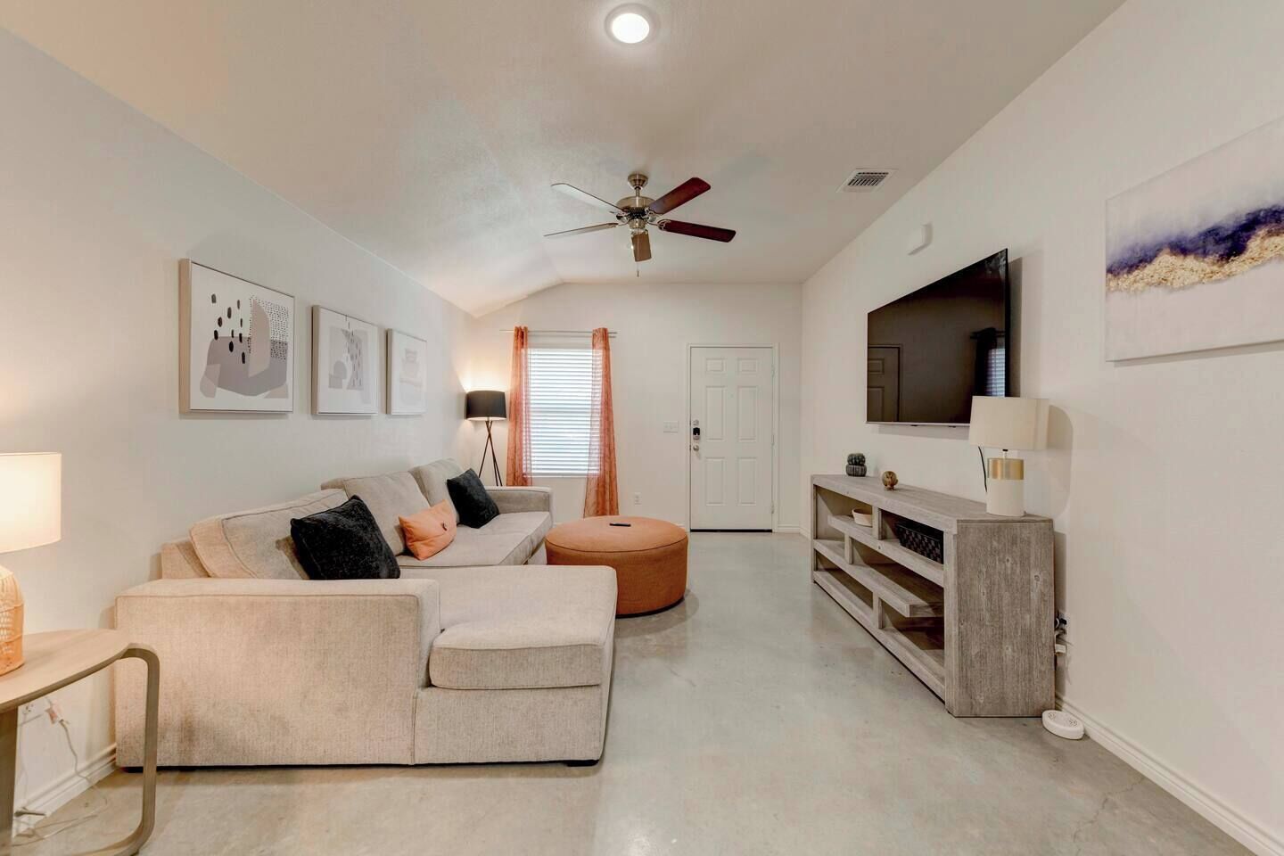 A living room with a sofa, ottoman, ceiling fan, and a TV on a wooden stand.