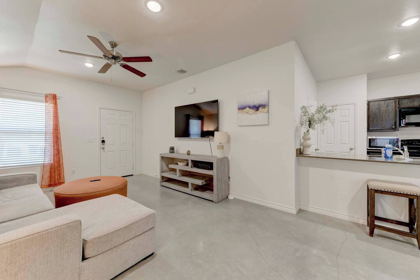 Un salon moderne comprenant un canapé, un pouf, un meuble de rangement pour appareils électroniques et un ventilateur de plafond.