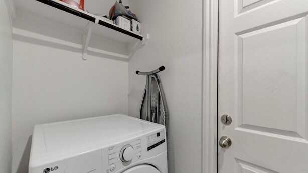 A laundry room with a white washing machine, a shelf with various items, and a door. - Your Getaway in Temple (Temple)