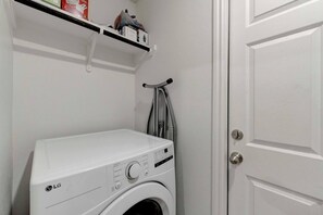 A laundry room with a white washing machine, a shelf with various items, and a door. - Your Getaway in Temple (Temple)