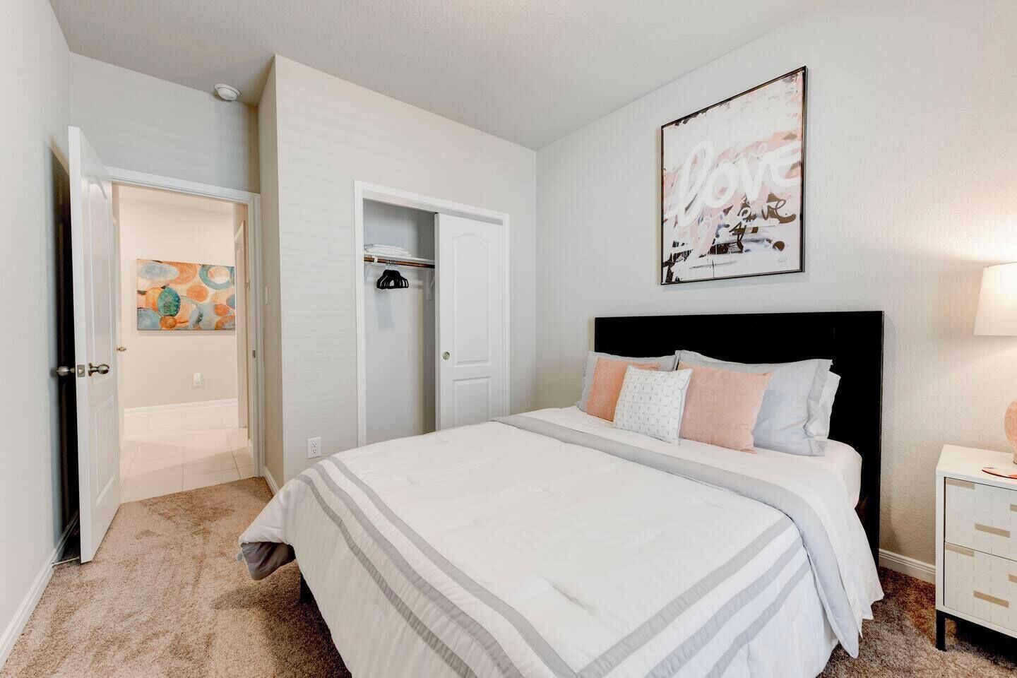 A bedroom with a bed, a nightstand, a closet, and a door leading to another room.