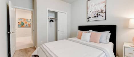 A bedroom with a bed, a nightstand, a closet, and a door leading to another room.