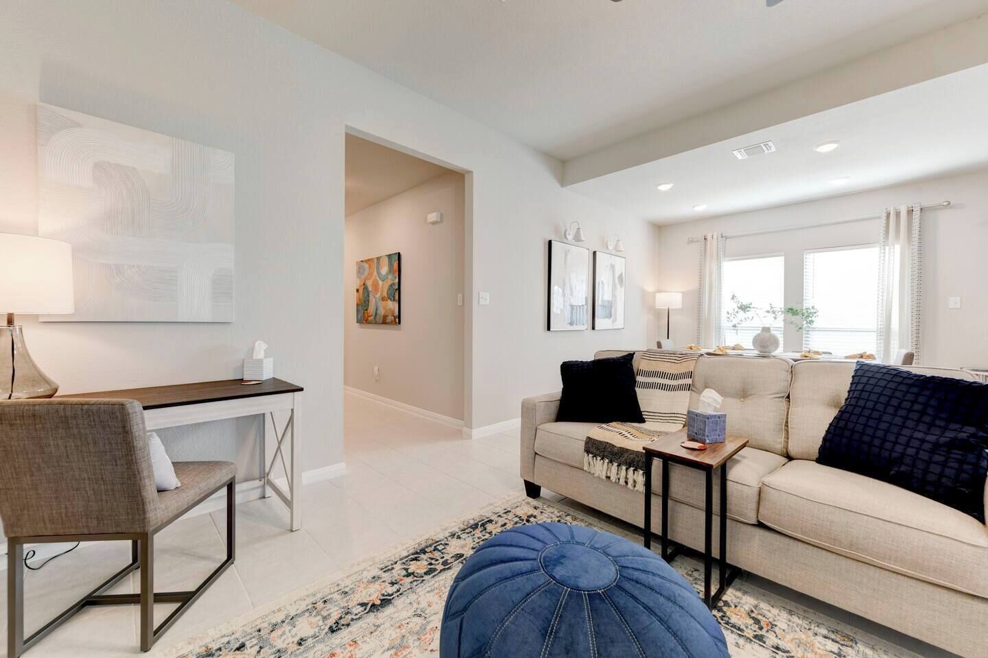 A modern living room with a sofa, coffee table, and a desk with a chair. There is a rug on the floor and artwork on the walls.