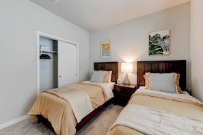 A hotel room with two beds, a bedside table with a lamp, a closet, and artwork on the walls.