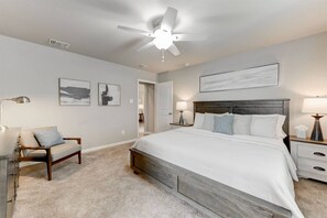 A bedroom with a large bed, a chair, a desk, and a ceiling fan.