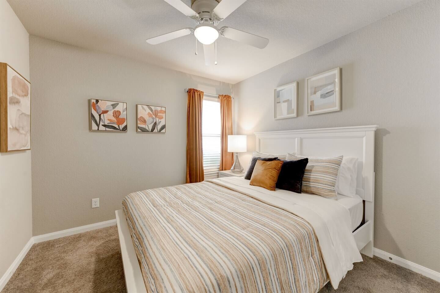 A bedroom with a bed, a ceiling fan, a nightstand, a lamp, and framed artwork on the wall.