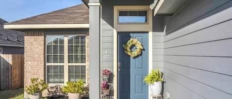 Une maison d’habitation avec une porte d’entrée bleue, une guirlande décorative, des plantes en pot et un petit porche.