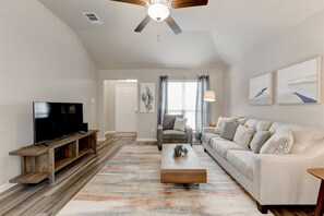A living room with a television, sofa, coffee table, and a ceiling fan.