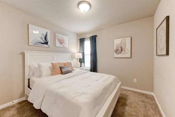 A bedroom with a large bed, a nightstand, a lamp, and artwork on the walls.