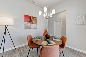 A dining area with a round table, orange chairs, a vase with flowers, and a chandelier.