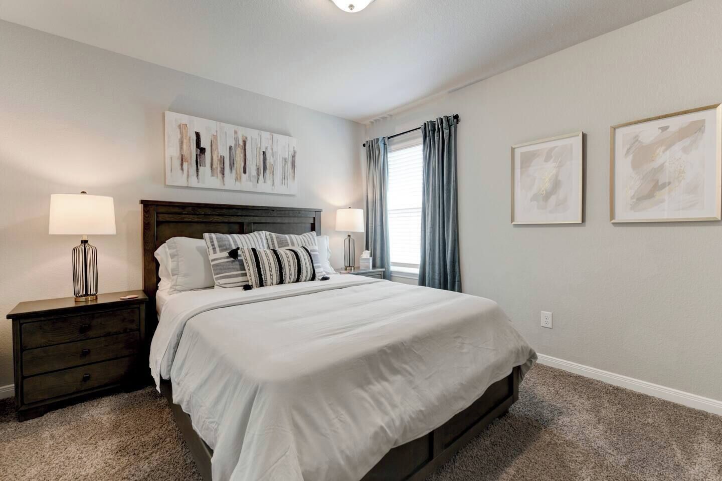 A bedroom with a bed, nightstands, a headboard, artwork, and a window with curtains.