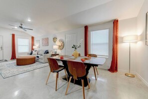 A modern living room with a dining area, featuring a sofa, a coffee table, a dining table with chairs, a floor lamp, and a ceiling fan.