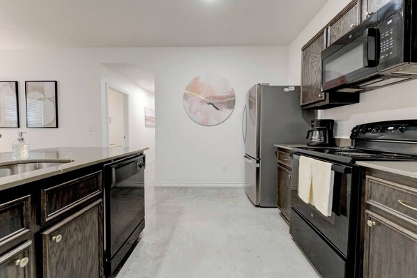 A kitchen with a refrigerator, stove, microwave, and a large circular artwork on the wall.