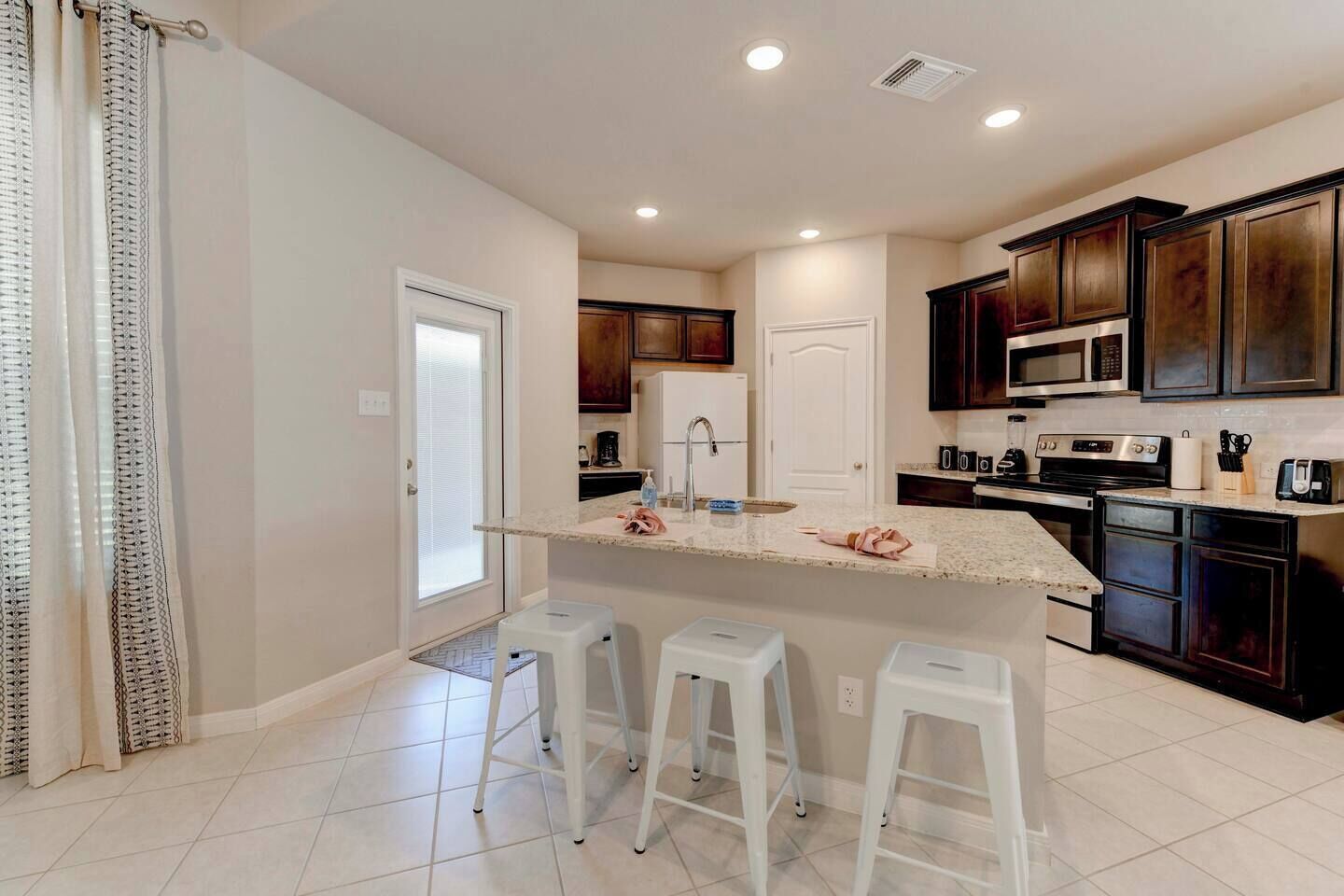 A modern kitchen with dark wood cabinets, a central island with stools, and a white countertop.