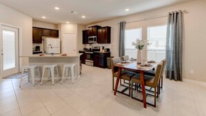 A modern kitchen with a central island, bar stools, and a dining table with chairs. - Brand New Home in Temple (Temple)