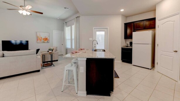A modern kitchen with a central island, a dining area with a sofa, and a TV. - Brand New Home in Temple (Temple)