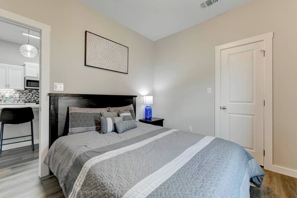 A bedroom with a bed, a nightstand, a lamp, a chair, and a door.